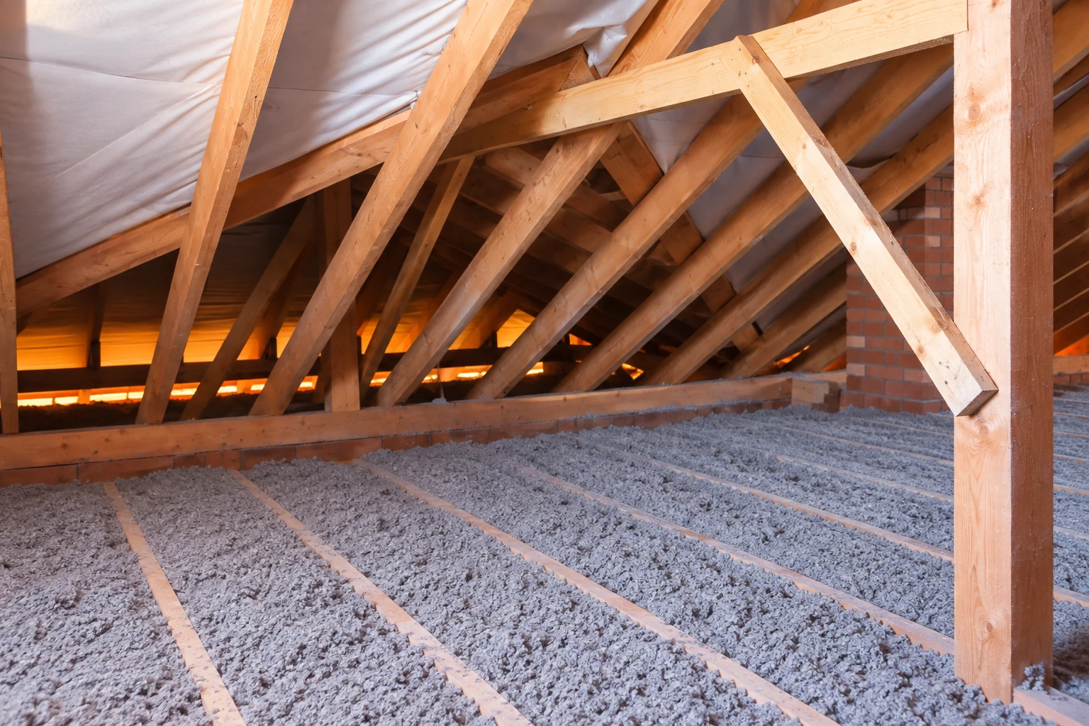 Blown-in insulation fills the attic floor between wooden joists beneath exposed roof trusses.