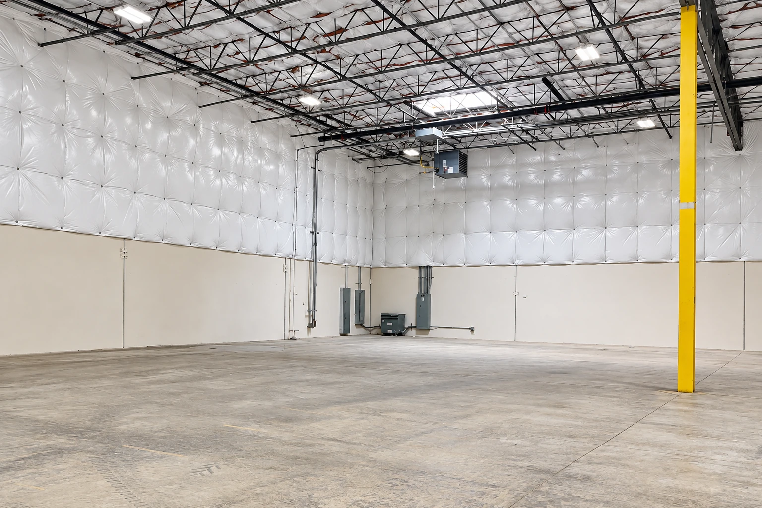 Empty commercial warehouse with white insulated walls and ceiling, exposed steel trusses, and a yellow support column.